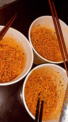 three bowls filled with noodles and chopsticks next to each other on a table