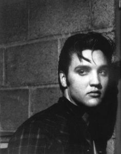 a black and white photo of a man in front of a brick wall with his head turned to the side