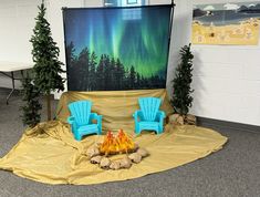 two blue chairs sitting in front of a fire pit with an aurora display behind them