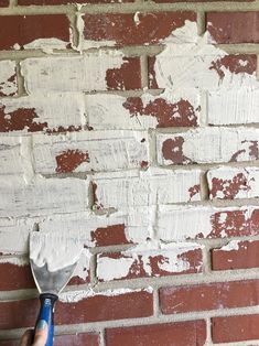 a brick wall with white paint being applied to it and a hand holding a brush