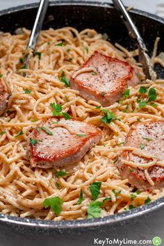 some meat and noodles are being cooked in a skillet with two tongs on the side