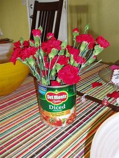 red carnations in a can on a table with plates and utensils