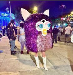 a woman in purple costume walking down the street at night with people standing around her