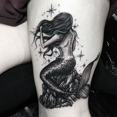 a black and white photo of a mermaid tattoo on the right thigh, with stars in the background