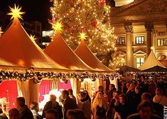 a large group of people standing in front of tents with christmas lights on the trees