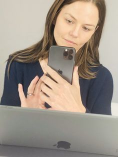 a woman looking at her cell phone in front of an apple laptop computer with the screen partially open