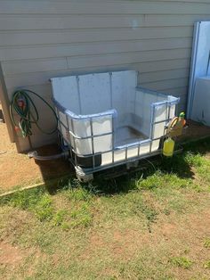 an empty trailer sitting in the grass next to a house with a hose attached to it