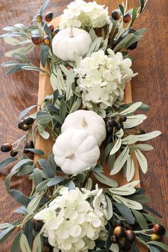 white pumpkins and greenery are arranged on a wooden board with olives, leaves and berries