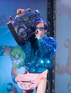 a woman with purple hair and glasses holding a boombox on top of her head