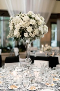 a vase filled with white flowers sitting on top of a table covered in glasses and plates