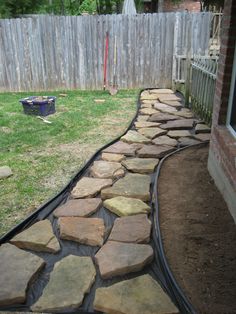 a stone path in front of a house next to a yard with a wooden fence