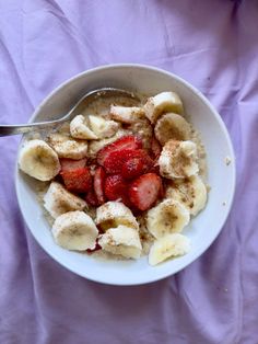 a bowl of cereal with bananas and strawberries in it on a purple cloth background