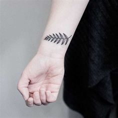 a small fern leaf tattoo on the left inner forearm and wristband is shown in black ink