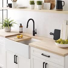 a kitchen with white cabinets and black faucets on the counter top, along with plants