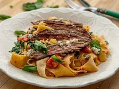 a white plate topped with pasta covered in meat and vegtables next to a fork