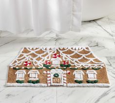 a gingerbread house door mat is on the floor next to a bathtub and shower curtain