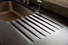 a stainless steel kitchen sink with black and white striped strips on the bottom, under a faucet