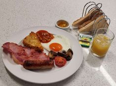 a white plate topped with bacon, eggs and toast next to a glass of orange juice