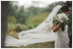 a woman in a wedding dress holding a bouquet with her veil flying over her head