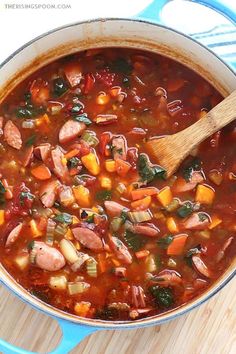 a pot filled with soup and vegetables on top of a wooden cutting board next to a spoon