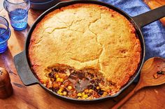 a skillet filled with food sitting on top of a wooden table next to water glasses