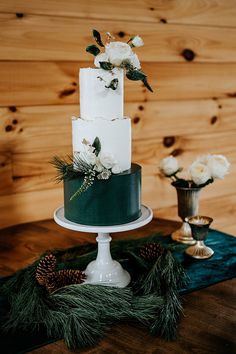 a white and green wedding cake sitting on top of a table next to pine cones