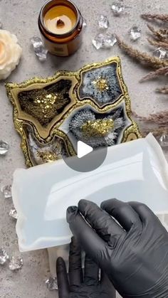 a person wearing black gloves and holding an object in front of some glass pieces with gold sequins on them