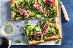 square pizza with asparagus, ham and green peppers on it next to a glass of water