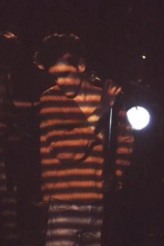 a man holding a microphone while standing in front of a light on a dark stage