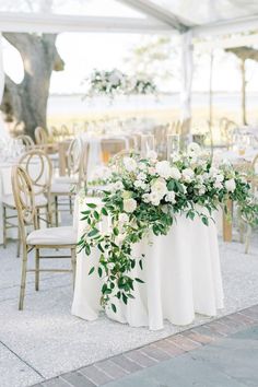 a table with white flowers and greenery is set up for an outdoor wedding reception