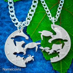 two silver necklaces with dolphins on them sitting next to a green leaf and blue background