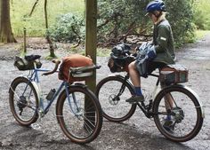 two people riding bikes in the woods with backpacks on their back and one person wearing a helmet