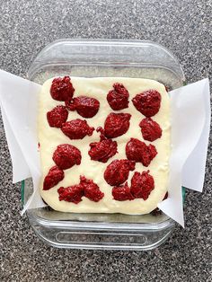 a square cake with white frosting and strawberries on top in a plastic container