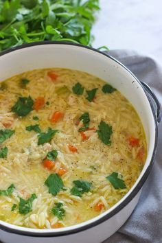 a white pot filled with chicken noodle soup on top of a gray cloth next to parsley