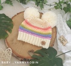 a crocheted hat with two pom - poms sits on top of a piece of wood