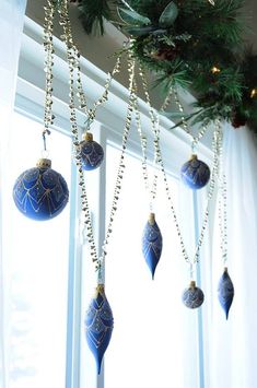 blue ornaments hanging from a window in front of a christmas tree