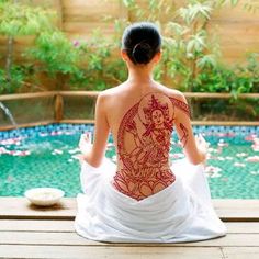 a woman sitting in front of a pool with tattoos on her back