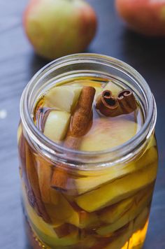 an apple cider in a glass jar with cinnamon stick, apples and other fruit