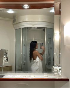 a woman in a white dress taking a selfie in front of a bathroom mirror