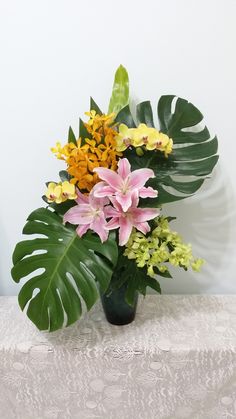 a vase filled with lots of colorful flowers on top of a white table covered in green leaves