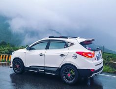 a white car parked on the side of a road in front of mountains and clouds