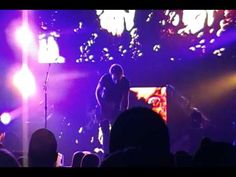 two men are standing on stage in front of a crowd at a concert with purple lighting