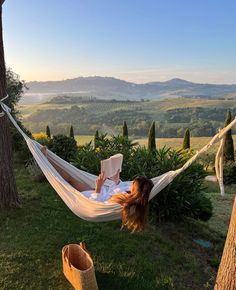 a woman laying in a hammock reading a book