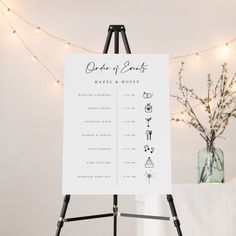 a white sign sitting on top of a easel next to a vase filled with flowers