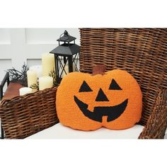 a knitted pumpkin pillow sitting on top of a wicker chair next to candles