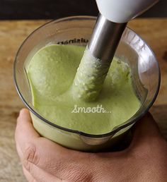 a hand holding a blender filled with green liquid