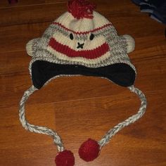 a knitted monkey hat with two pom poms sitting on top of a wooden floor