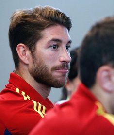 a close up of a man with a beard wearing a red shirt and looking off to the side