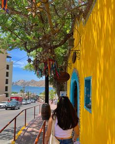 a woman walking down the sidewalk next to a yellow building with colorful decorations hanging from it's roof