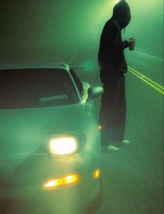 a man standing next to a car in the dark with his headlamps on